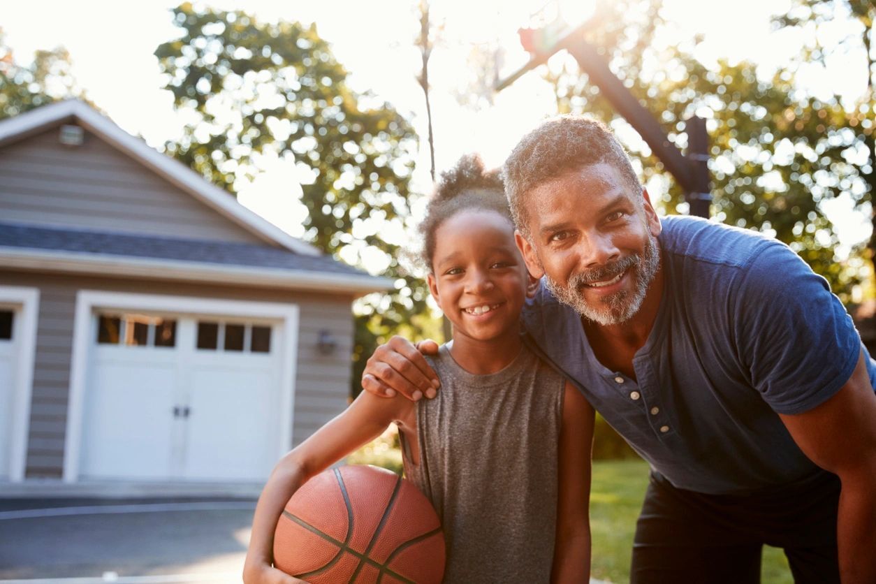 Portrait Of Father And Son Playing Basketball On Driveway